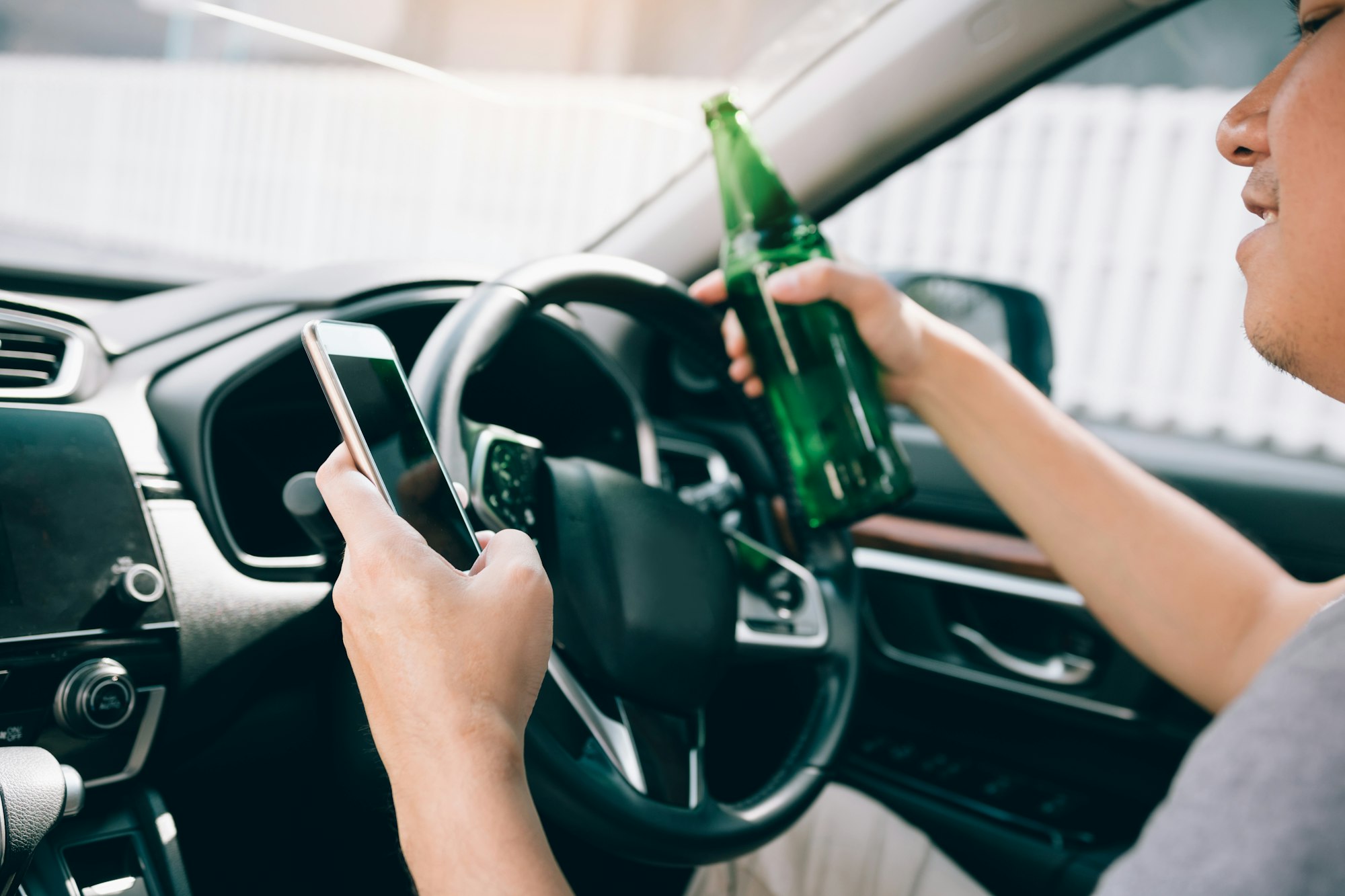 Asian men drink alcohol in the car and using mobile phones while driving.